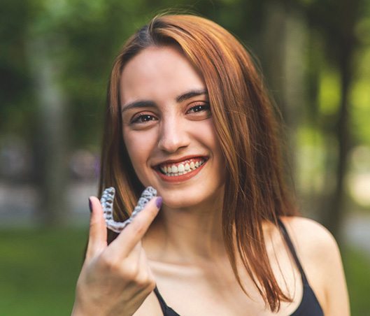 Woman with reddish hair smiling and holding Invisalign aligner