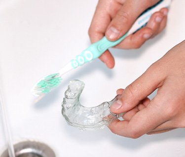 Cleaning Invisalign aligner with toothbrush in sink