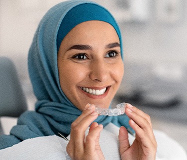 Smiling woman in dental chair holding Invisalign aligner