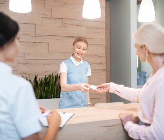 Smiling woman paying for clear aligner treatment at dental office