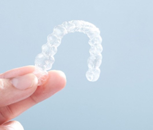 Patient holding up clear aligner against blue background