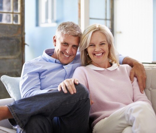 Smiling older man and woman sitting on couch after getting dental bridges in Fort Worth