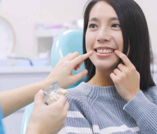 Woman in dental chair pointing to her smile after a dental cleaning in Fort Worth