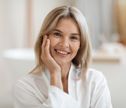 Woman in white bathrobe smiling and touching her cheek
