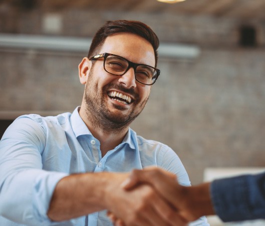 Man in denim shirt with glasses shaking hands with another person