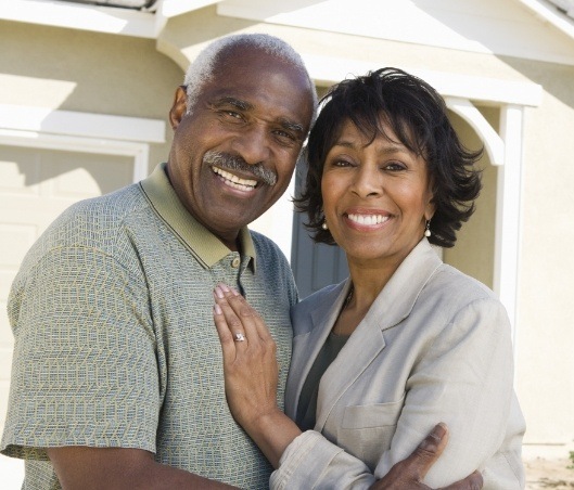 Smiling senior man and woman with dentures in Fort Worth holding each other outdoors