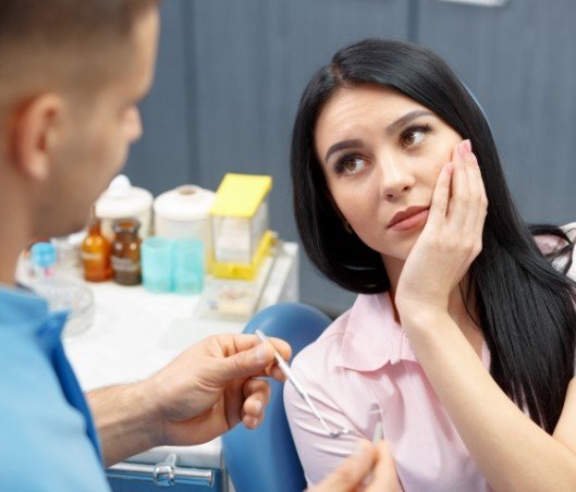 Woman holding her cheek in pain while seeing emergency dentist in Fort Worth