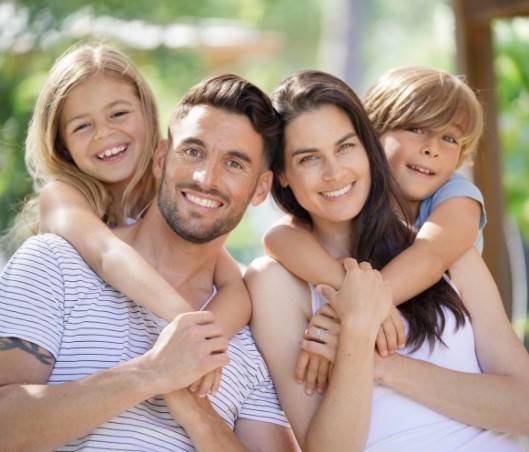 Family of four smiling outdoors after seeing their family dentist in Fort Worth