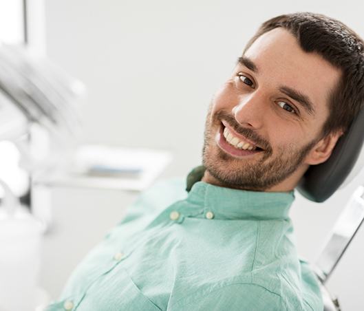 Man with facial hair leaning back in dental chair and smiling