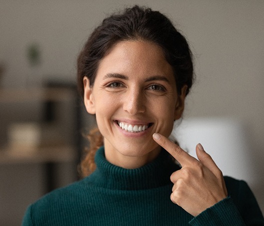Woman in dark green sweater pointing to her smile