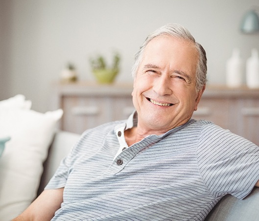 Senior man in striped shirt sitting on couch and smiling