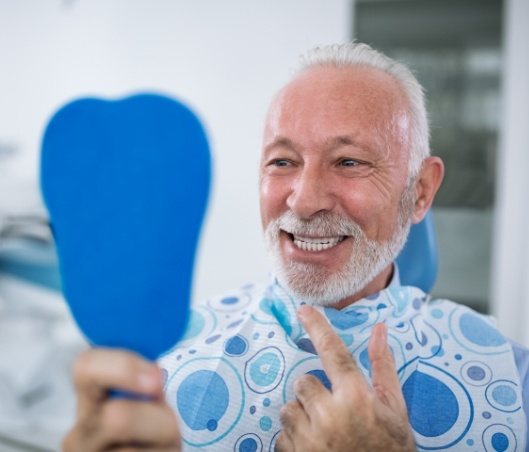 Senior man seeing his new smile in mirror after restorative dentistry in Fort Worth