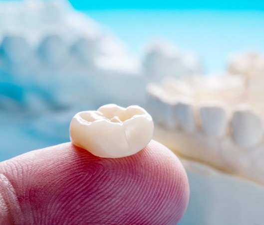 a finger holding a dental crown