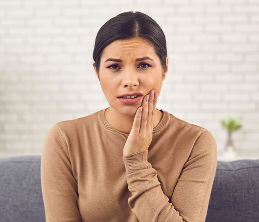 Woman who needs tooth extractions in Fort Worth holding her cheek in pain